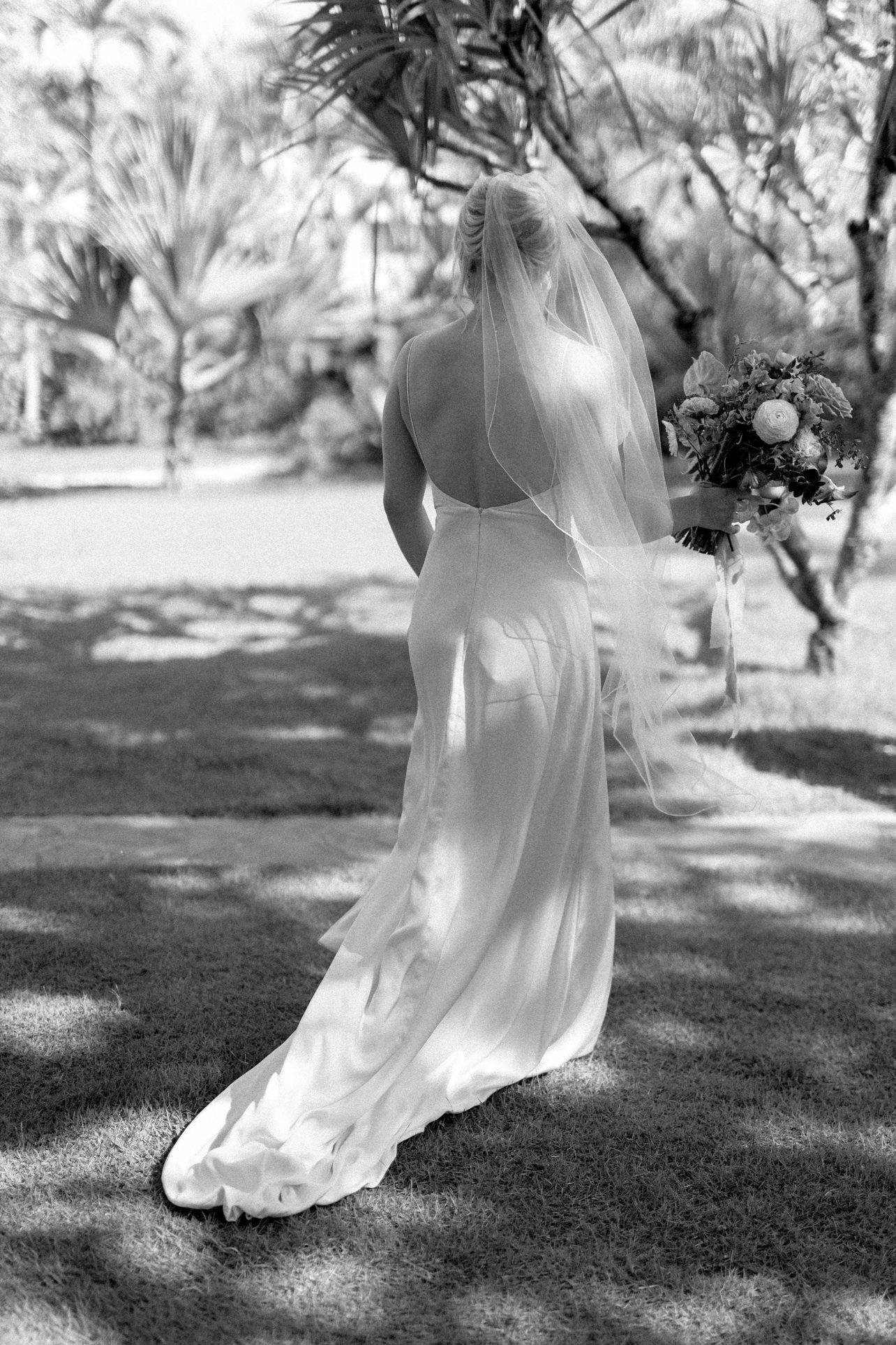 Novia de espaldas con velo en el jardín, en blanco y negro