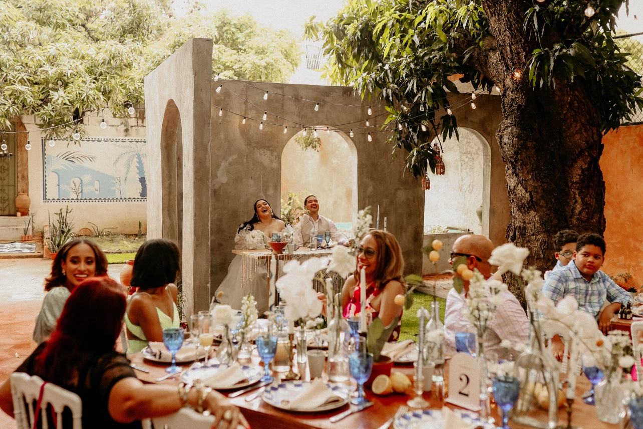 Novios e invitados disfrutando la recepción bajo árboles y luces
