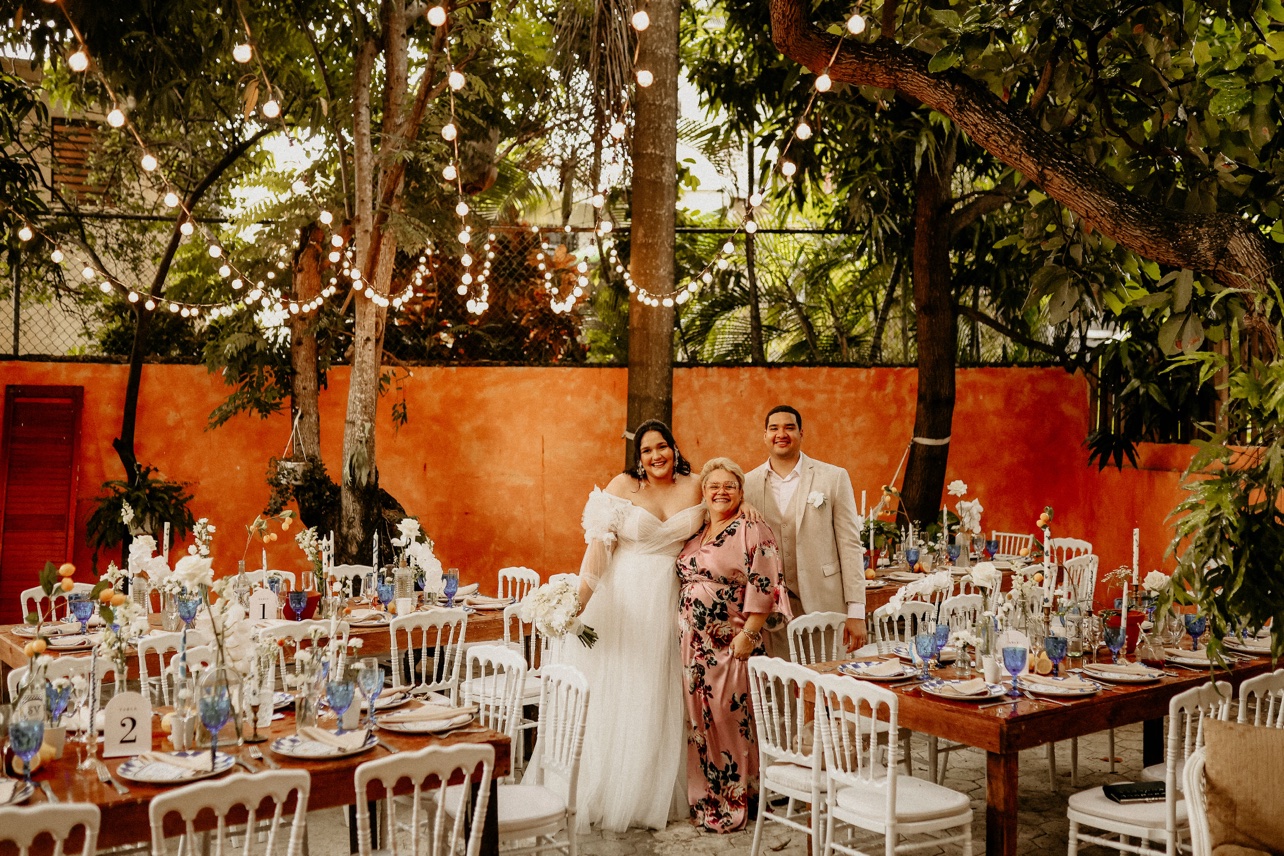Novios posando con una invitada entre las mesas de la recepción