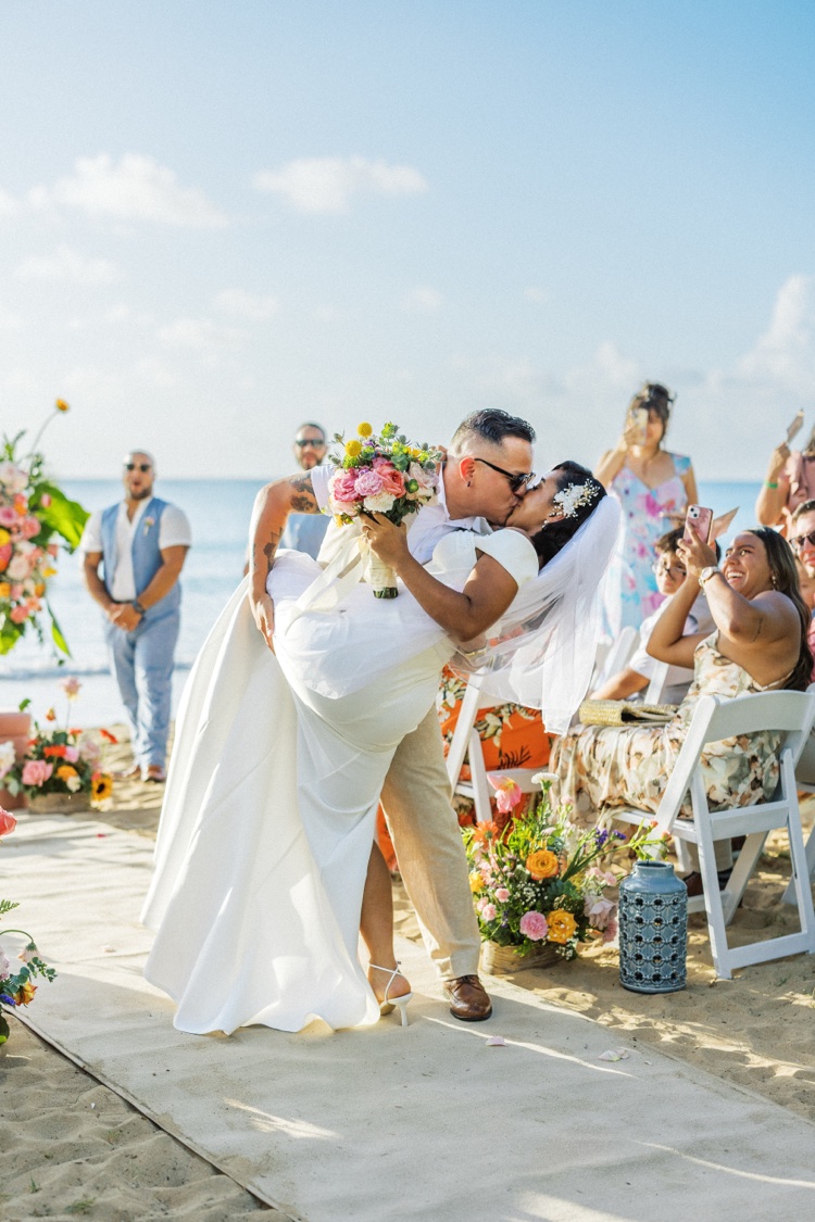 Novio cargando y besando a la novia durante la ceremonia en la playa