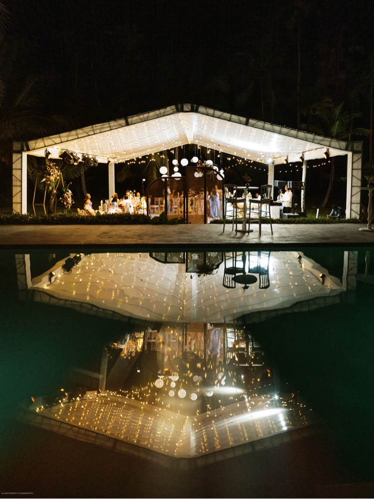 Carpa de recepción iluminada y reflejada en la piscina por la noche